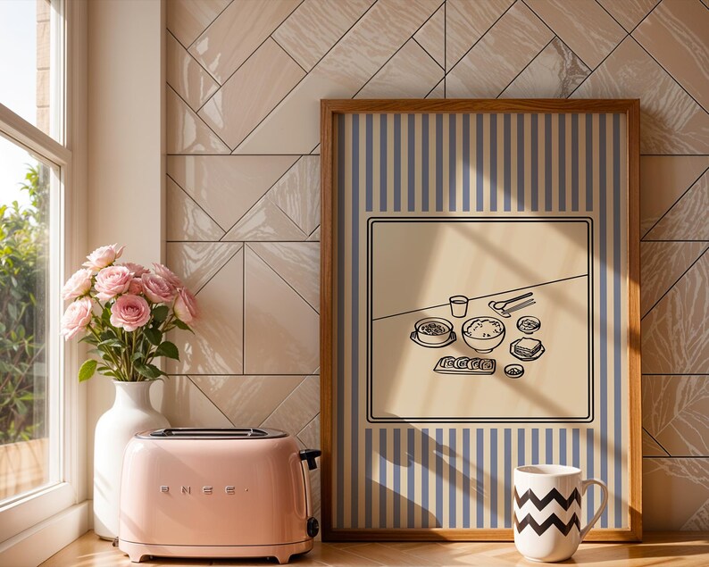 Puede incluir: Una tostadora SMEG rosa se encuentra junto a una ventana con un jarr&oacute;n de rosas rosas. Una impresi&oacute;n enmarcada presenta un fondo beige con una ilustraci&oacute;n en blanco y negro de una comida. Una taza blanca con zigzags negros est&aacute; frente a la impresi&oacute;n.