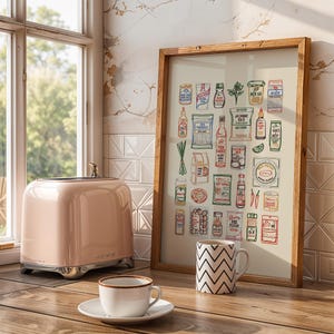 May include: A pink toaster with chrome accents sits on a wooden surface next to a framed print of food items. A white mug with a black zigzag pattern and a teacup and saucer are also on the table. The print is in a wooden frame.