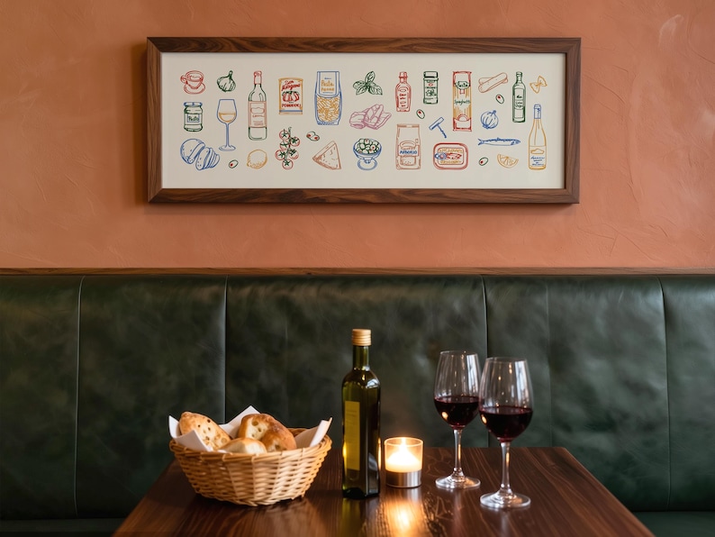 May include: A dining scene featuring a framed artwork of colorful food illustrations above a table. The table holds a basket of bread, a bottle of olive oil, a lit candle, and two wine glasses filled with red wine. The background includes a green leather booth and a reddish-brown wall.