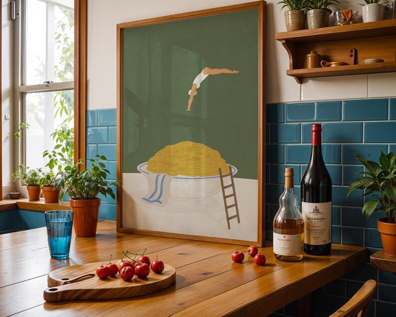 May include: A framed art print depicts a person diving into a bowl of spaghetti. A wooden cutting board with cherries, a blue glass, and two bottles of wine sit on a wooden table. The art print has a wooden frame.
