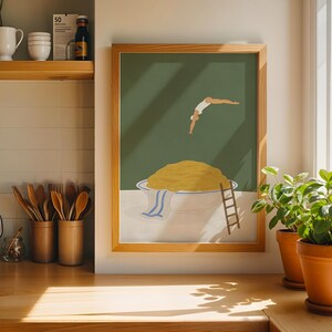 May include: A framed art print depicts a person diving into a bowl of spaghetti. The artwork features a green background, a large bowl of pasta, and a small wooden ladder. The frame is made of light-colored wood.