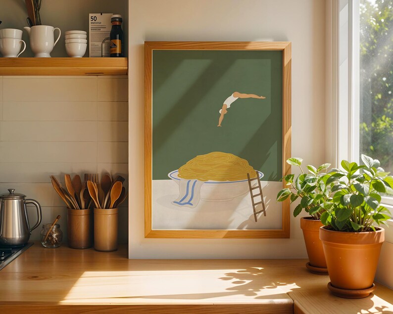 May include: A framed art print depicts a person diving into a bowl of spaghetti. The artwork features a green background, a large bowl of pasta, and a small wooden ladder. The frame is made of light-colored wood.