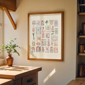 May include: A framed print featuring a colorful illustration of various Asian grocery items. The artwork includes depictions of sauces, spices, and packaged goods, all arranged in a grid-like pattern. The print is displayed in a kitchen setting, with a wooden frame and a neutral background.