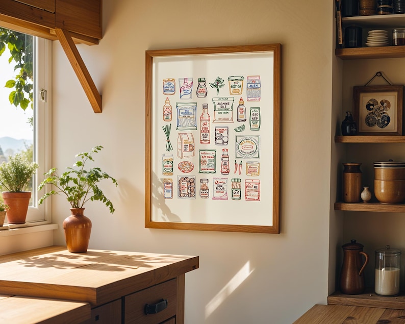May include: A framed print featuring a colorful illustration of various Asian grocery items. The artwork includes depictions of sauces, spices, and packaged goods, all arranged in a grid-like pattern. The print is displayed in a kitchen setting, with a wooden frame and a neutral background.