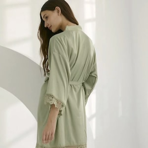 May include: A sage green satin robe with a lace trim. The robe has a tie belt and long sleeves.