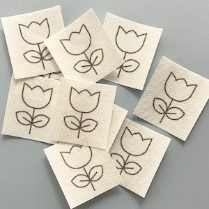 May include: Nine white fabric squares with a brown outline of a tulip flower on each.