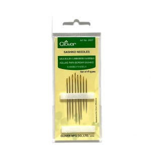 May include: A package of Clover Sashiko needles. The package is clear plastic with a yellow and green label. The label reads "Sashiko Needles" in English, French, Spanish, and German. The package contains a set of four gold-colored needles.