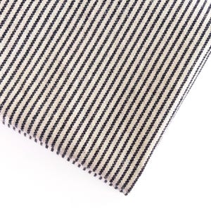 May include: Close-up of a folded fabric with a cream-colored background and evenly spaced, dark navy blue vertical stripes. The fabric has a textured appearance, suggesting a woven material. The stripes create a classic, timeless pattern.