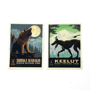 May include: Two rectangular art prints featuring mythical creatures. One depicts a brown wolf-like creature howling at a full moon, with text "Shunka Warakin". The other shows a black dog-like creature with text "Keelut".