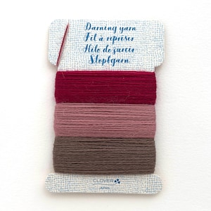 May include: A rectangular card wrapped with three distinct shades of darning yarn in dark red, dusty rose, and brown. The card features the text Darning yarn, Fil à repriser, Hilo de zurcir, Stopfgarn and the Clover Japan logo at the bottom.