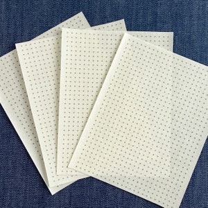 May include: Four white sheets of fabric with a small, evenly spaced dot pattern. The fabric is folded in a fan shape.