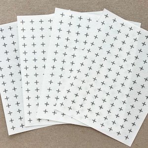 May include: Five white sheets of paper with a repeating pattern of black plus signs.