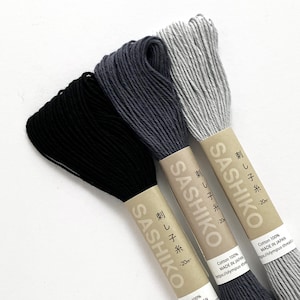 May include: Three spools of Sashiko thread in black, gray, and light gray. Each spool is labeled "Sashiko" and "刺し子糸" with the text "20m" on the label.