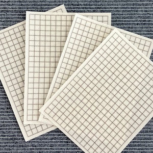 May include: Four white gridded fabric squares with brown lines. The squares are stacked on top of each other.