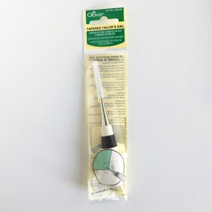 May include: A Clover Tapered Tailor's Awl in a clear plastic package. The awl has a silver metal tip, a white handle, and a black grip. The package includes text in multiple languages, including "TAPERED TAILOR'S AWL".