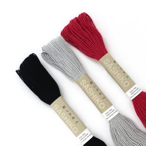 May include: Three spools of Sashiko thread in black, gray, and red. Each spool has a paper label with Japanese text and the brand name. The thread is cotton and made in Japan.
