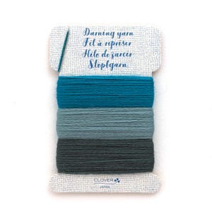 May include: A rectangular card holding three shades of darning yarn in teal, light blue, and dark gray. The card features the text Darning yarn, Fil à repriser, Hilo de zurcir, Stopfgarn, and Clover Japan, with a small needle icon on the left side.