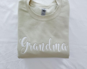 May include: A light beige sweatshirt with the word "Grandma" embroidered in white on the front.
