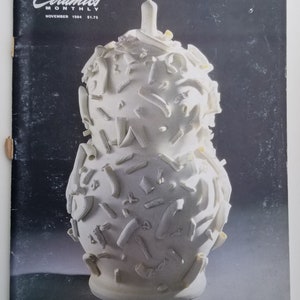 May include: A white ceramic vase with a textured surface. The vase is decorated with small, white ceramic pieces that resemble pasta.