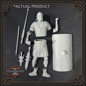 May include: Gray plastic model kit of a Roman legionary.  The unassembled kit includes the torso, legs, arms, head, shield, sword, spear, and other accessories.  The product is shown against a dark gray background.  The text '*ACTUAL PRODUCT*' is visible above the kit.  The logo 'THE FORGE OF HISTORY 3D Resin Figures' is at the bottom.