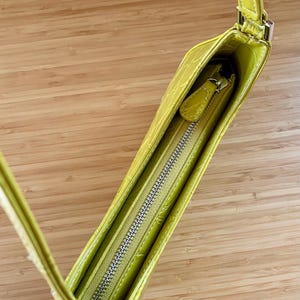 Puede incluir: Un bolso verde lima con un patr&oacute;n texturizado similar al de un cocodrilo. El bolso tiene una correa larga y delgada y una cremallera plateada. El interior es visible, revelando un forro verde lima a juego.