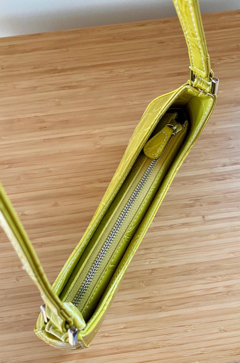 Puede incluir: Un bolso verde lima con un patr&oacute;n texturizado similar al de un cocodrilo. El bolso tiene una correa larga y delgada y una cremallera plateada. El interior es visible, revelando un forro verde lima a juego.
