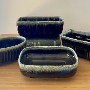 May include: Four ceramic planters in varying shapes and sizes. The planters are dark brown with a green and white glaze around the rims. One planter has vertical ridges, and another has a rectangular shape with three square cutouts.