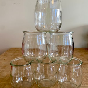 May include: Six clear glass jars stacked in a pyramid shape. The jars are empty and have a rounded bottom.