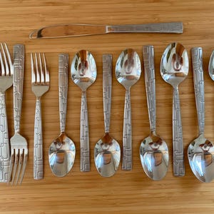 May include: A set of stainless steel flatware including four forks, five spoons, and one knife. Each piece features a polished finish and a textured handle with a geometric pattern of raised lines and rectangles along the stem.