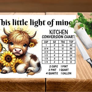 Puede incluir: Tabla de conversión de cocina con una ilustración de una vaca de las Tierras Altas con girasoles. La tabla incluye medidas en tazas, onzas, cucharadas y cucharaditas, además de conversiones de volumen.