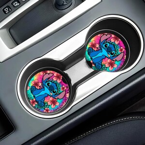 May include: Two car coasters with a colorful tie-dye background and a blue Stitch character from Lilo & Stitch. The coasters are in a car cup holder.