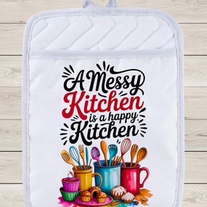 Peut inclure: Manique de cuisine blanche matelassée avec le texte "A Messy Kitchen is a happy Kitchen". Elle présente des illustrations colorées d'ustensiles de cuisine, de cupcakes et de tasses. Un accessoire de cuisine amusant et fonctionnel.