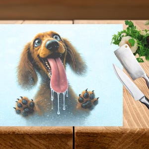May include: A rectangular cutting board featuring a cartoon illustration of a brown dachshund with a long pink tongue and water droplets. A cleaver and knife are next to fresh vegetables on a wooden surface.