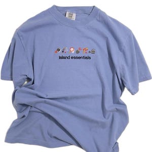May include: A light blue t-shirt with a row of colorful embroidered icons and the text "Island essentials" in black.