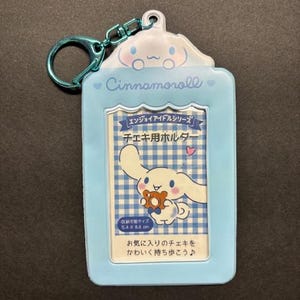 May include: A light blue Cinnamoroll photo holder with a matching keychain. The holder features a cartoon character and Japanese text. The photo area is 5.4 x 8.6 cm.