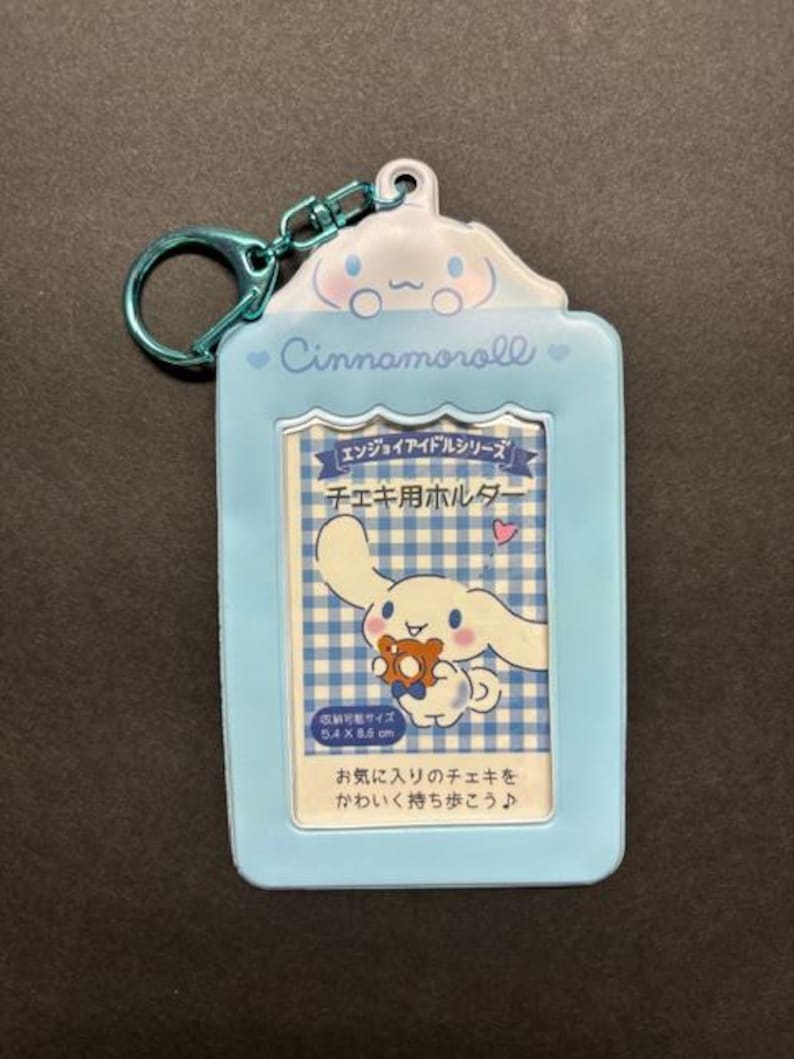 May include: A light blue Cinnamoroll photo holder with a matching keychain. The holder features a cartoon character and Japanese text. The photo area is 5.4 x 8.6 cm.