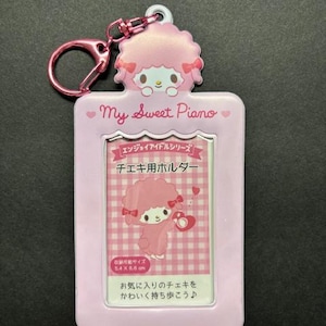 May include: A pink photo holder keychain featuring a cartoon sheep character with a pink bow. The holder has a rectangular frame with the text "My Sweet Piano" and Japanese text. The keychain includes a pink clasp.