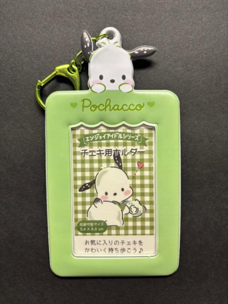 May include: A green Pochacco keychain with a cartoon image of Pochacco. The keychain has a green frame with the word "Pochacco" and Japanese text. The frame holds a picture of Pochacco with a camera. The keychain is 5.4 x 8.6 cm.
