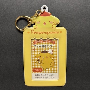 May include: Yellow Pompompurin photo holder with a gold keychain. The holder features a cartoon character design and Japanese text. The holder is designed to hold a photo that is 5.4 x 8.5 cm.