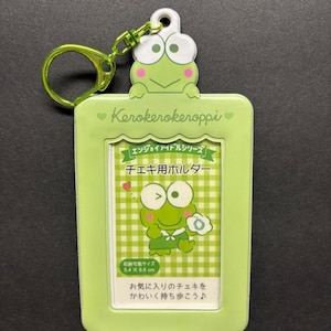 May include: A light green Keroppi photo holder with a matching green keyring. The holder features a Keroppi frog design and Japanese text. The holder is designed to hold photos that are 5.4 x 8.6 cm.