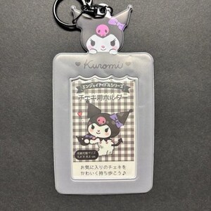 May include: A gray Kuromi-themed keychain with a cartoon character design. The keychain features a clear plastic holder with a printed image of Kuromi and Japanese text. The holder is designed to hold a small card, measuring 2.1 x 3.4 inches.