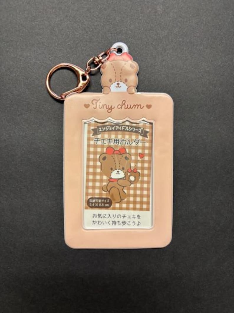 May include: A light pink Tiny Chum photo holder with a bear design, a gold-colored keychain, and Japanese text. The holder features a bear illustration holding a cherry and a checkered background. The text reads "Tiny Chum".
