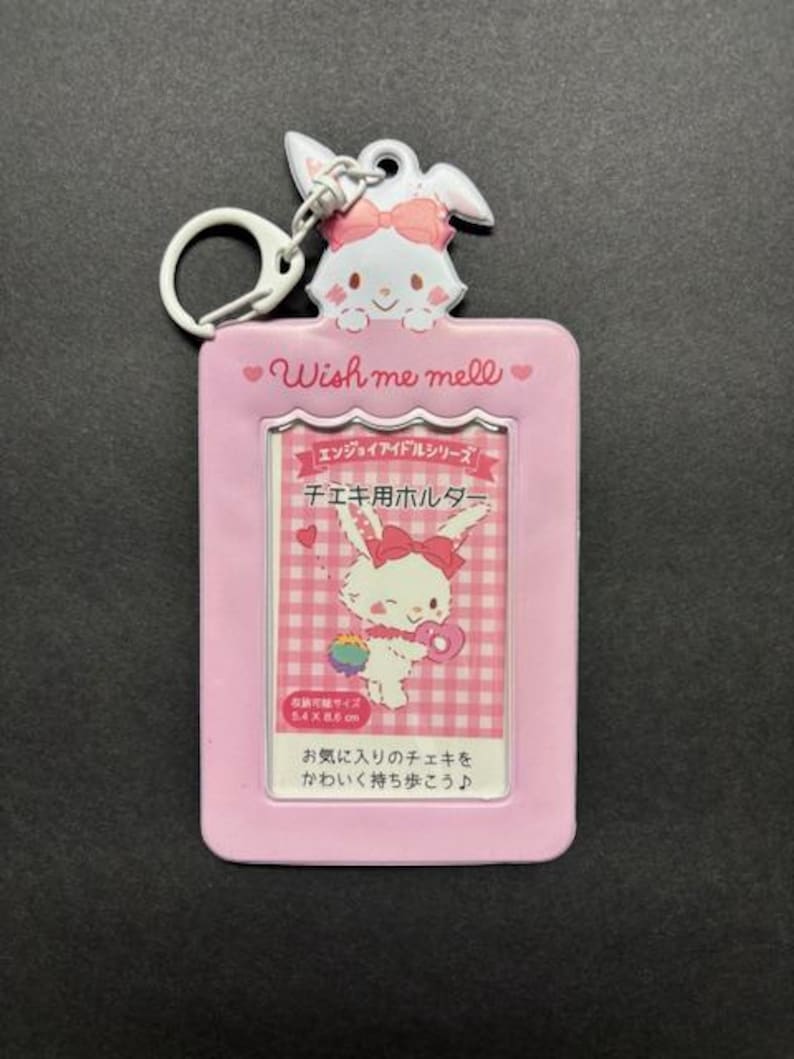 May include: A pink photo holder with a cartoon bunny design, a metal keyring, and the text "Wish me mell." The holder features a clear window for a photo and Japanese text. The holder measures 5.4 x 8.6 cm.