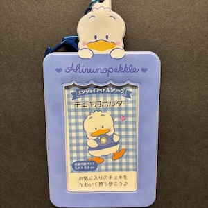 May include: A light blue photo holder featuring a cartoon duck character. The holder has a rectangular shape with rounded edges and a small duck-shaped charm at the top. The text "Ahinunopekkle" is printed on the holder.