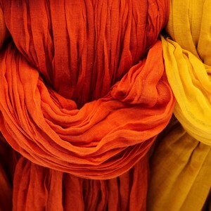 Peut inclure: Gros plan sur trois écharpes drapées dans des tons orange et jaune. Les écharpes sont faites d'un tissu léger, avec une texture et des plis visibles. Les couleurs vont d'un orange-rouge profond à un jaune vif, créant une palette chaleureuse.