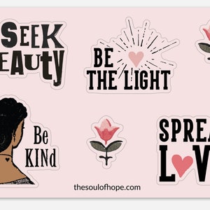 May include: A set of six pink and black stickers with inspirational messages. The stickers feature a woman with a heart tattoo, flowers, and the words "Seek Beauty", "Be the Light", "Be Kind", and "Spread Love".