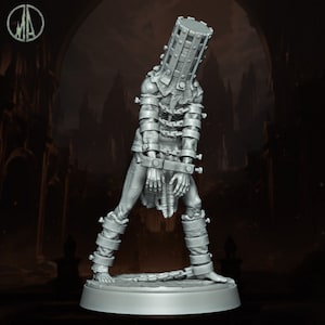Puede incluir: Una figura en miniatura gris y detallada de una persona que lleva una jaula de metal sobre la cabeza y encadenada en las muñecas y los tobillos. La figura está de pie sobre una base redonda.