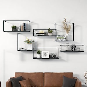 May include: Five black metal floating shelves with various plants, books, and decorative items. The shelves are mounted on a white wall.