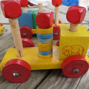 May include: A wooden toy train with red and yellow wheels, a red and yellow block with an elephant design, and a stack of colorful blocks. The train is made of wood and has a simple design.