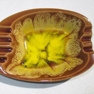 May include: A brown and yellow ceramic ashtray with a wavy rim and a yellow center. The ashtray has a glazed finish.